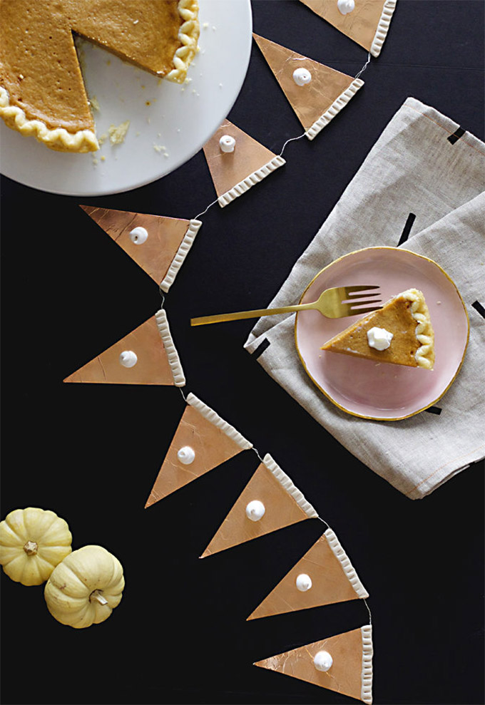 A garland made out of paper slices of pumpkin pie. On the top left there is a real pumpkin pie with a slice cut out. On the right there is a slice of real pumpkin pie with a dollop of icing on the top.