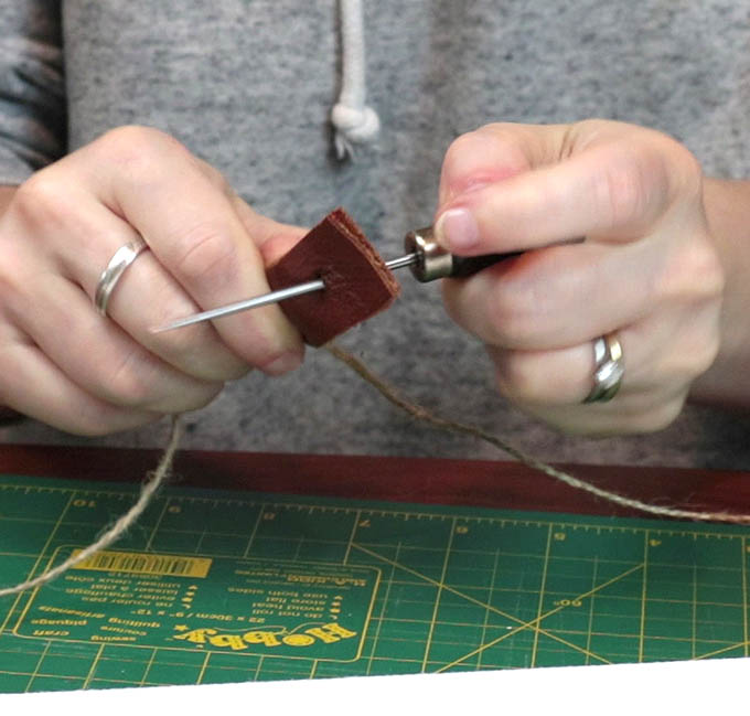 Punching a hole with an awl in the leather tab in order to hang my DIY wall hanging - this step is optional in this project!