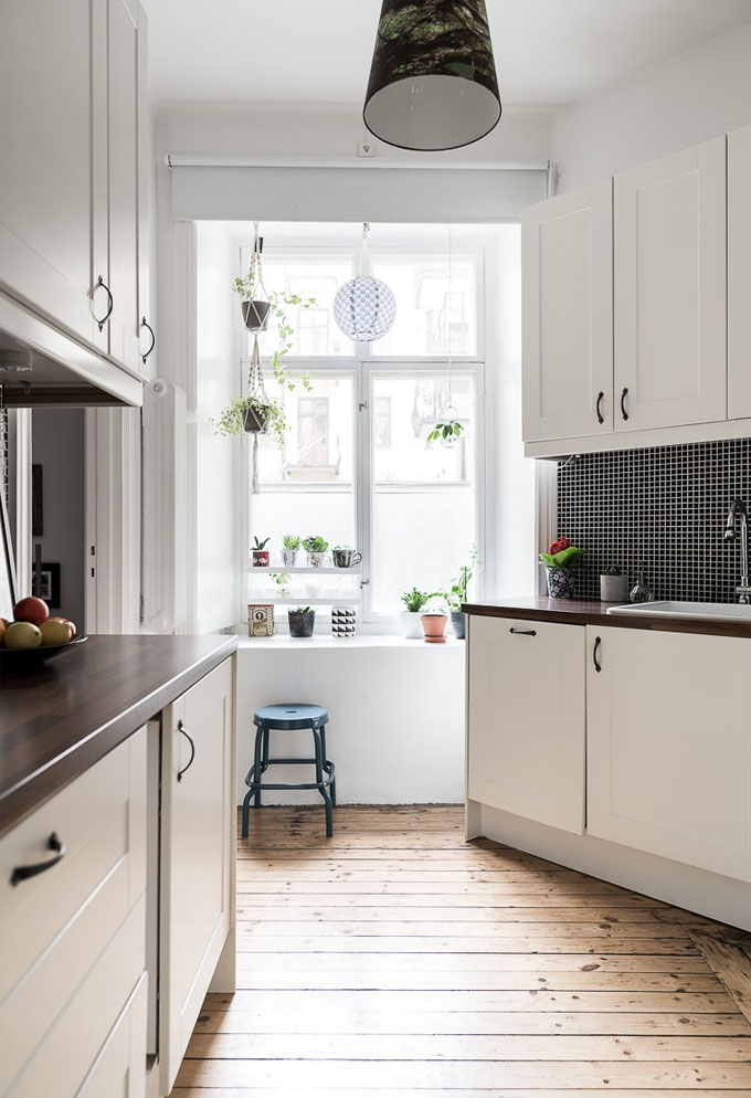 A typical scandinavian kitchen, with wood floors, white cabinets and a dark tiled backsplash