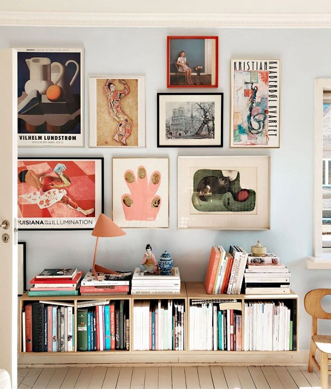playful gallery wall on light blue wall above a bookshelf