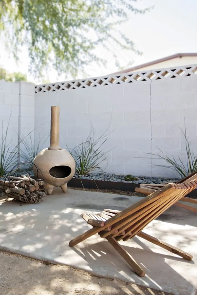 beautiful minimal fire pit area with a tan colored chiminea and two teak chairs