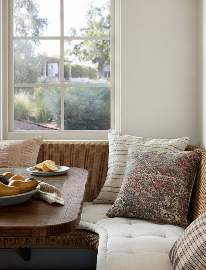 eclectic throw pillow mix on a rattan bench with a cream colored seat cushion
