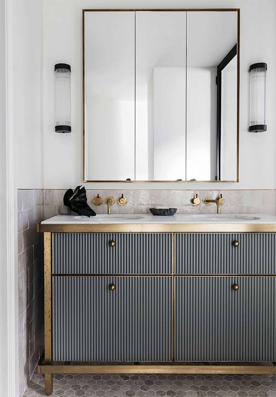 fluter bathroom cabinets framed with gold, coordinating gold mirror, gold knobs and gold faucets. black metal accent sconces