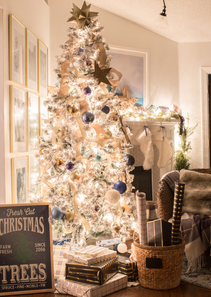 white flocked christmas tree with gfits in front, tree decorated with blue balls and ribbons